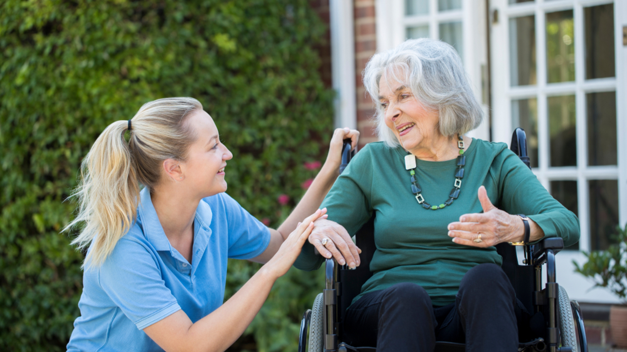 Carer,Pushing,Senior,Woman,In,Wheelchair,Outside,Home